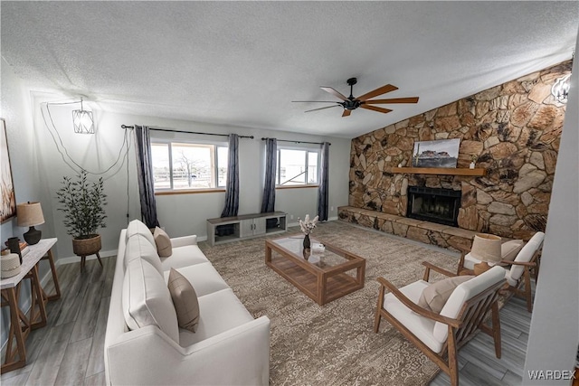 living area with a textured ceiling, a fireplace, wood finished floors, a ceiling fan, and vaulted ceiling