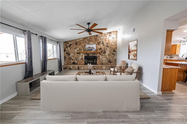 living room featuring wood finish floors, a fireplace, vaulted ceiling, a textured ceiling, and ceiling fan