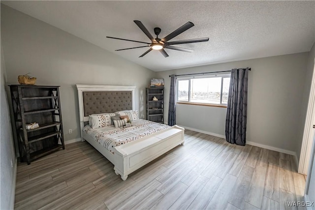 bedroom with vaulted ceiling, a textured ceiling, baseboards, and wood finished floors