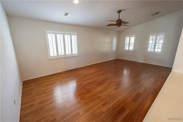 empty room featuring ceiling fan, vaulted ceiling, wood finished floors, and visible vents
