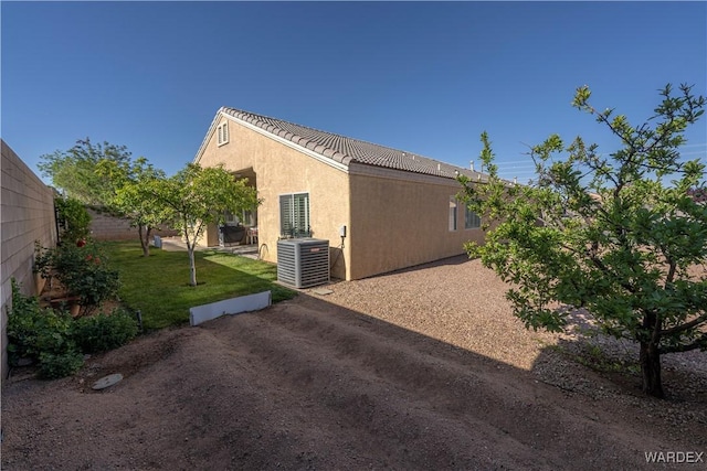 view of home's exterior with central AC, fence, stucco siding, a tiled roof, and a lawn