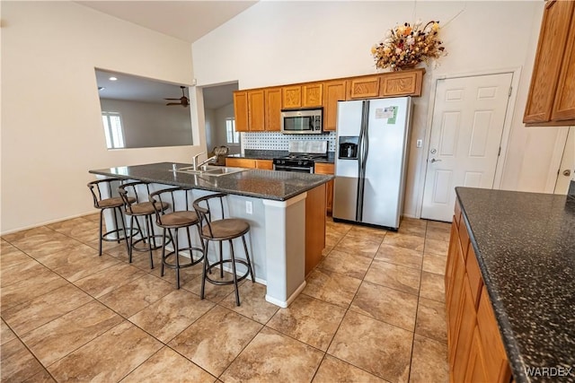 kitchen featuring a kitchen breakfast bar, brown cabinets, a sink, dark stone countertops, and stainless steel appliances