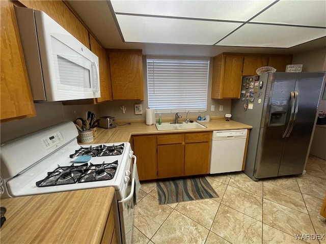 kitchen with light tile patterned floors, light countertops, brown cabinetry, a sink, and white appliances