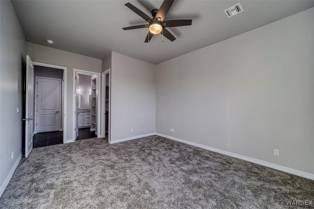 unfurnished bedroom with ceiling fan, visible vents, baseboards, dark colored carpet, and ensuite bath