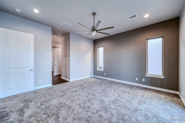 spare room featuring a barn door, visible vents, baseboards, ceiling fan, and dark carpet