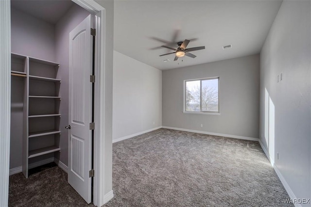 empty room with ceiling fan, dark colored carpet, visible vents, and baseboards