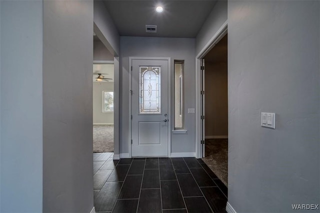 foyer entrance featuring dark colored carpet, visible vents, ceiling fan, and baseboards