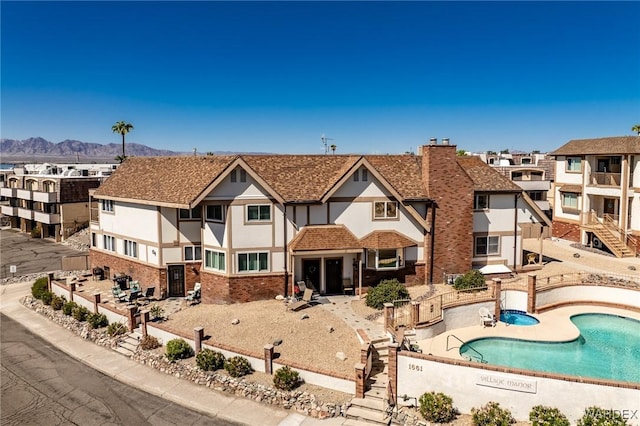 exterior space featuring a community pool, a shingled roof, brick siding, a residential view, and stucco siding