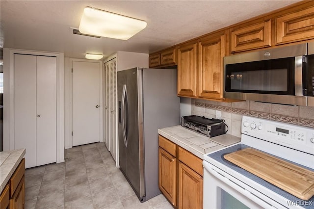 kitchen with stainless steel appliances, brown cabinetry, tile countertops, and decorative backsplash