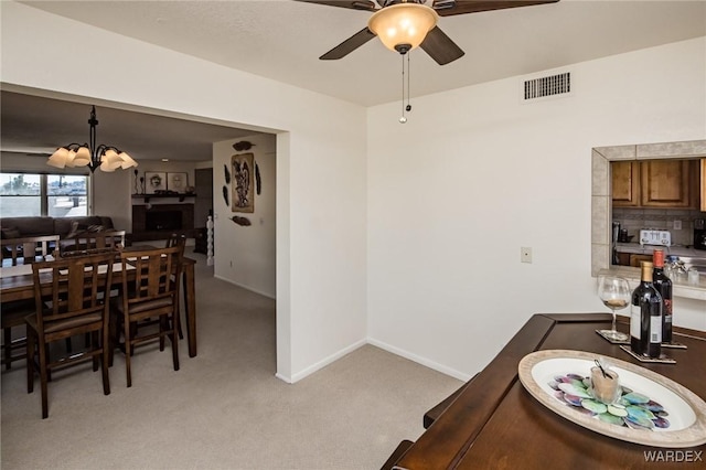 dining area with light carpet, ceiling fan with notable chandelier, visible vents, and baseboards