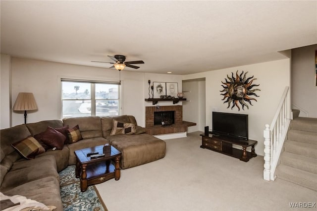 carpeted living room with a brick fireplace, ceiling fan, and stairway