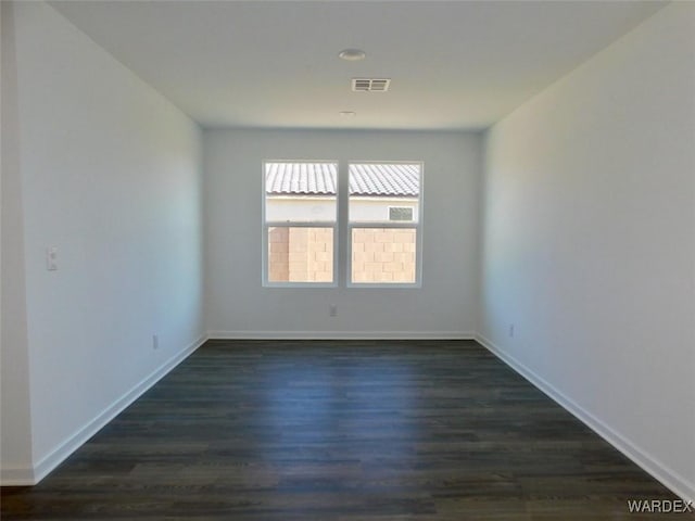 empty room featuring dark wood-style floors, visible vents, and baseboards