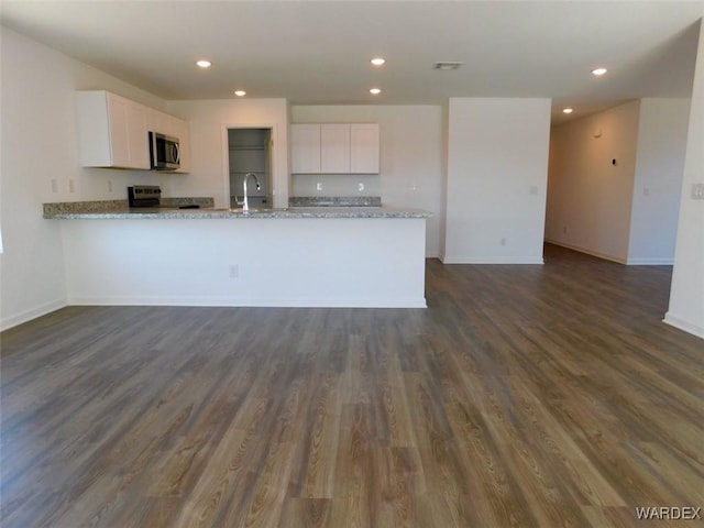 kitchen featuring white cabinets, appliances with stainless steel finishes, a peninsula, light stone countertops, and a sink