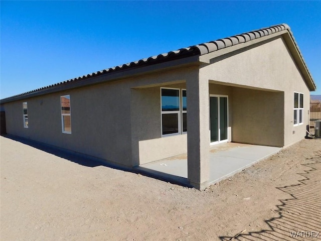 rear view of property with stucco siding, a tiled roof, central AC, and a patio