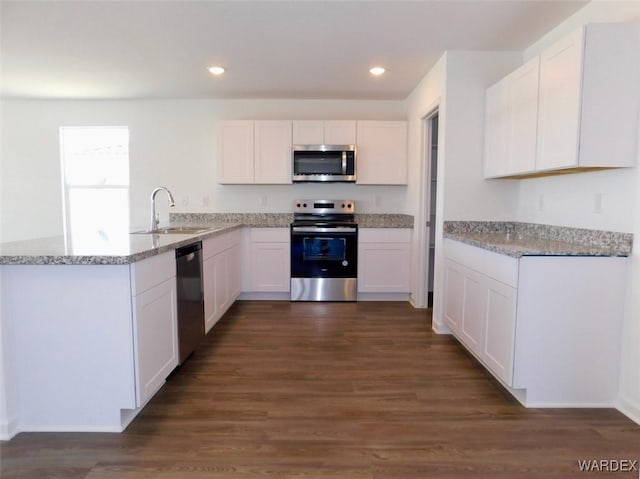 kitchen featuring light stone counters, a peninsula, a sink, white cabinets, and appliances with stainless steel finishes