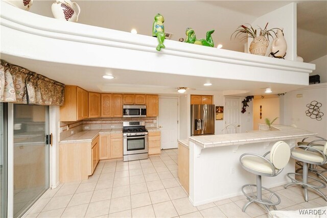 kitchen featuring a breakfast bar area, light tile patterned floors, stainless steel appliances, tile counters, and backsplash