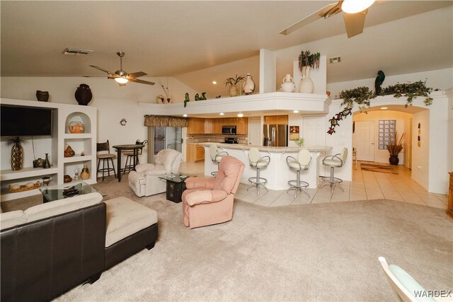 living area featuring arched walkways, light tile patterned floors, light colored carpet, visible vents, and ceiling fan