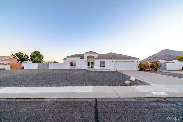 mediterranean / spanish house with a garage, concrete driveway, fence, a mountain view, and stucco siding