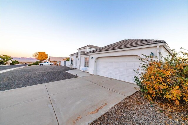 view of front of home with an attached garage, a tiled roof, concrete driveway, and stucco siding