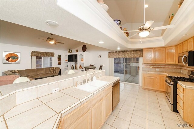 kitchen with a tray ceiling, tile countertops, stainless steel appliances, light brown cabinetry, and open floor plan