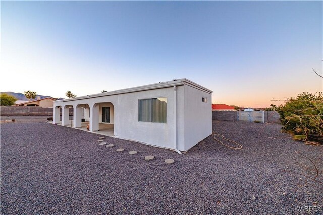 back of property at dusk with a fenced backyard, a patio, and stucco siding