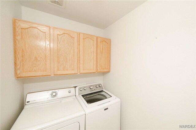 washroom featuring washing machine and dryer, cabinet space, and visible vents