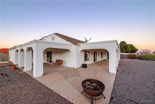 back of property at dusk with fence, a patio, a fire pit, and stucco siding