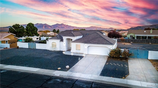 view of front facade featuring a fenced front yard, a mountain view, a garage, concrete driveway, and a gate