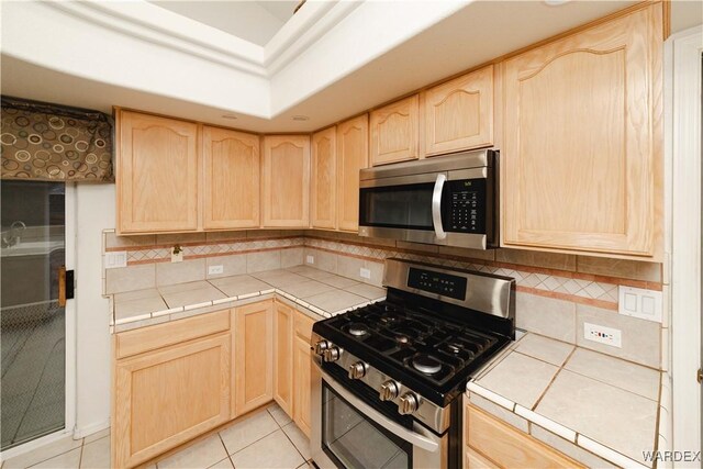 kitchen with tile countertops, light brown cabinetry, and appliances with stainless steel finishes