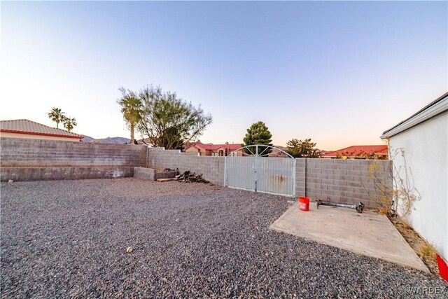 yard at dusk with a fenced backyard, a gate, and a patio