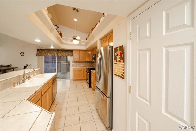 kitchen with light tile patterned floors, tile counters, a raised ceiling, appliances with stainless steel finishes, and a sink