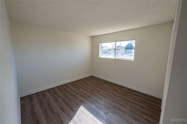 empty room with dark wood-style floors, a textured ceiling, and baseboards