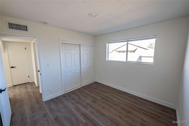 unfurnished bedroom featuring a closet, visible vents, dark wood finished floors, and baseboards