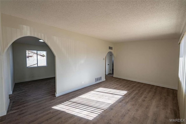 spare room featuring visible vents, arched walkways, dark wood finished floors, and a textured ceiling