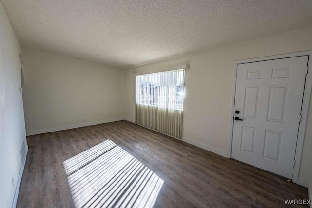 empty room with a textured ceiling, baseboards, and dark wood-type flooring