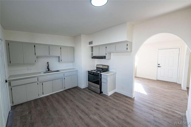 kitchen with gray cabinetry, dark wood-style flooring, a sink, light countertops, and stainless steel range with gas stovetop