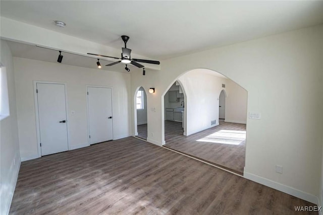 unfurnished bedroom featuring arched walkways, visible vents, baseboards, and wood finished floors