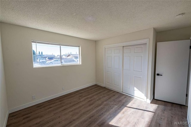 unfurnished bedroom with dark wood-style floors, a textured ceiling, baseboards, and a closet