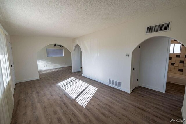 empty room featuring arched walkways, dark wood-style floors, and visible vents