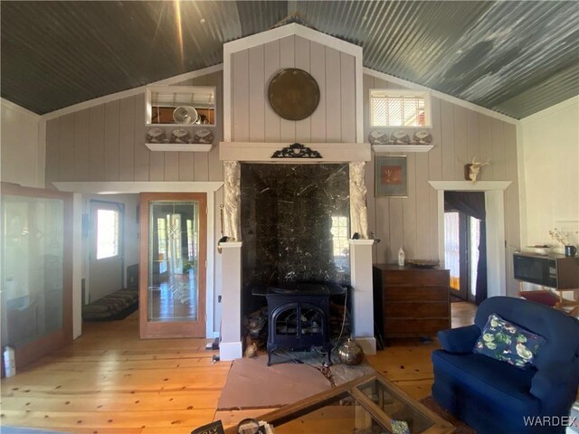 living area featuring high vaulted ceiling, wood finished floors, a wood stove, and wooden walls