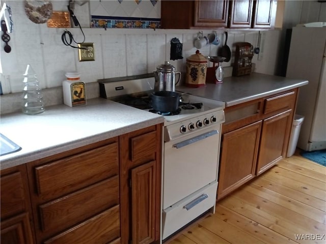 kitchen with white range, brown cabinetry, light countertops, and freestanding refrigerator