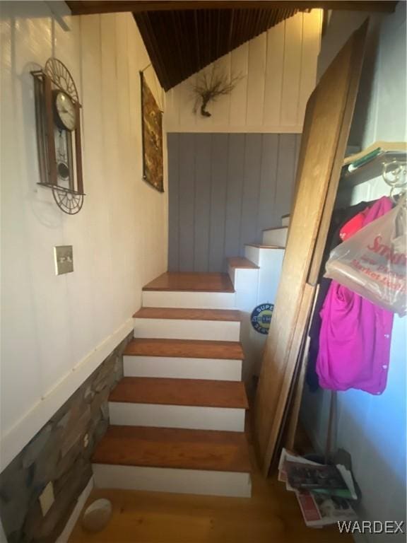 stairway with wainscoting, vaulted ceiling, and wooden walls