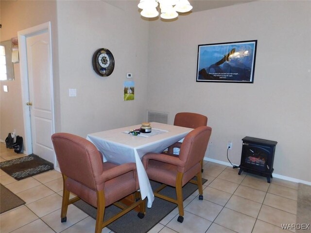 dining space featuring a wood stove, visible vents, a notable chandelier, and light tile patterned floors