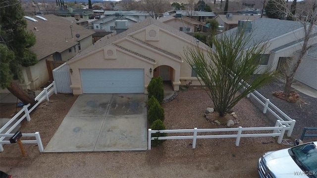 view of front facade with stucco siding, an attached garage, fence, a residential view, and driveway