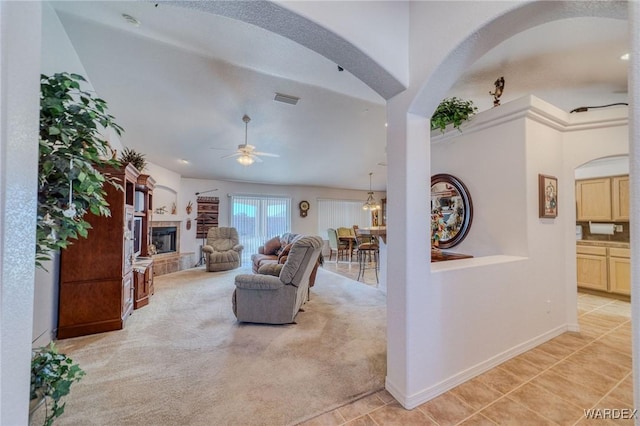 living area with a tile fireplace, light carpet, arched walkways, and baseboards