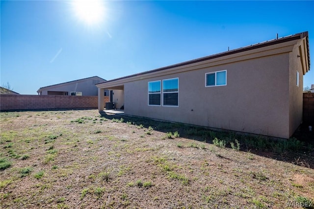 back of property with central AC, fence, and stucco siding