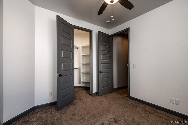 unfurnished bedroom featuring baseboards, a spacious closet, dark carpet, and a ceiling fan