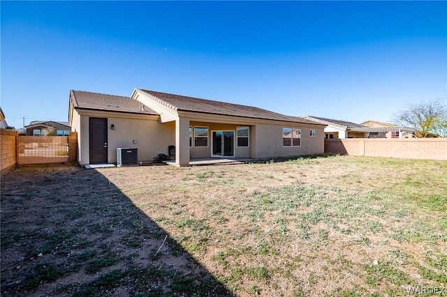 rear view of house with a fenced backyard, a lawn, central AC unit, and stucco siding