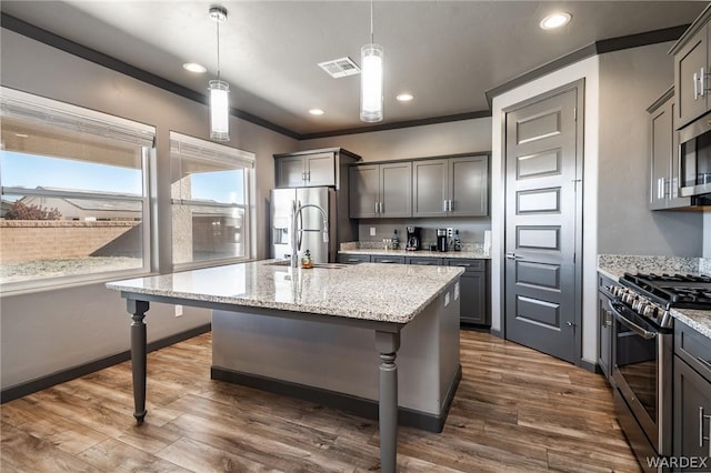 kitchen with an island with sink, appliances with stainless steel finishes, decorative light fixtures, a kitchen bar, and a sink