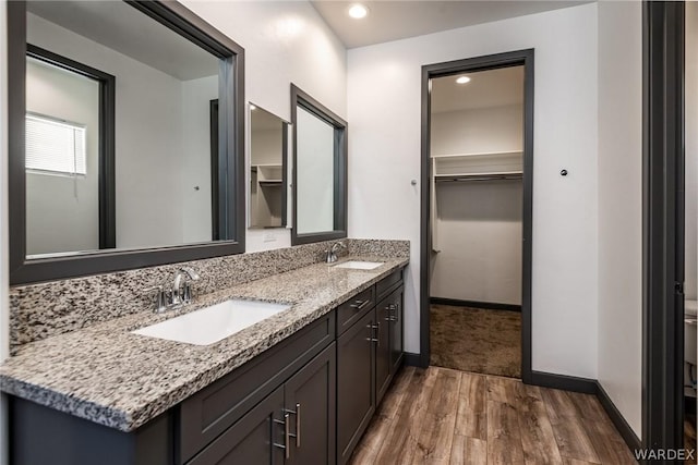 bathroom with double vanity, wood finished floors, a sink, and a walk in closet